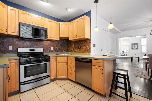 kitchen featuring sink, light hardwood / wood-style flooring, tasteful backsplash, decorative light fixtures, and stainless steel appliances