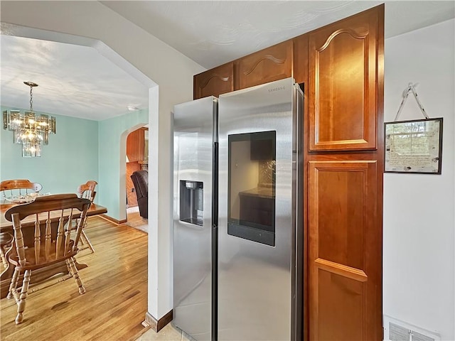 kitchen with hanging light fixtures, a notable chandelier, stainless steel fridge, and light hardwood / wood-style flooring