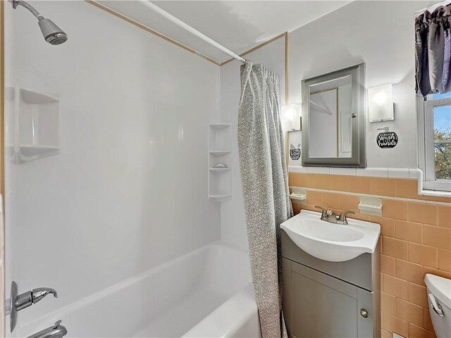 full bathroom featuring vanity, shower / bathtub combination with curtain, toilet, and tile walls