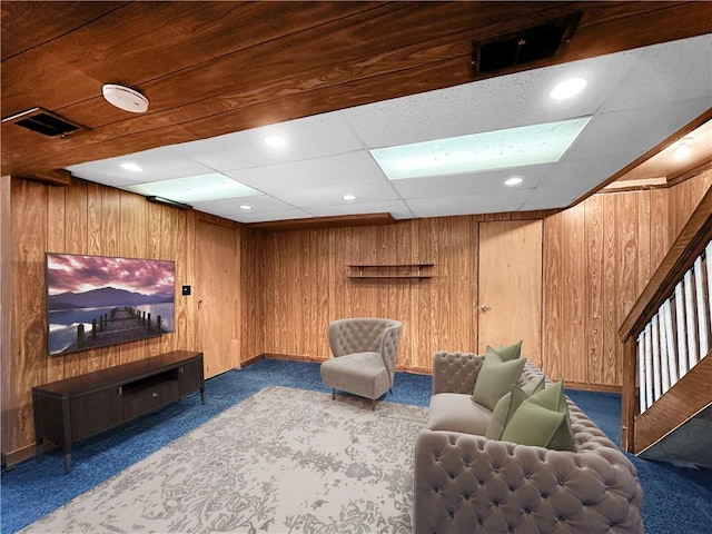 carpeted living room with a drop ceiling and wooden walls