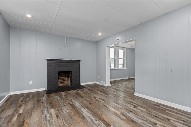 unfurnished living room with wooden walls, dark hardwood / wood-style flooring, and a brick fireplace