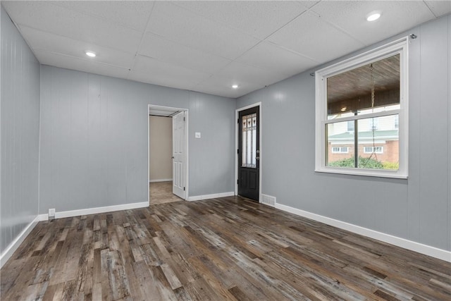 spare room with wood walls, a drop ceiling, and dark hardwood / wood-style floors