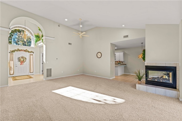 unfurnished living room featuring light carpet, high vaulted ceiling, a tile fireplace, and ceiling fan