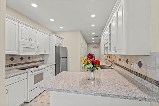 kitchen with kitchen peninsula, light stone counters, white cabinetry, sink, and white appliances