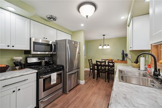 kitchen featuring stainless steel appliances, sink, an inviting chandelier, white cabinets, and light hardwood / wood-style floors