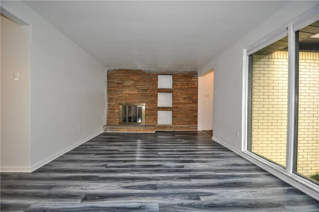 unfurnished living room with brick wall, dark wood-type flooring, and a fireplace