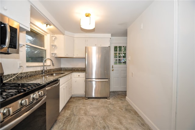 kitchen with white cabinetry, appliances with stainless steel finishes, sink, and dark stone counters