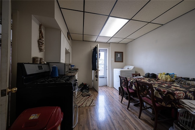 kitchen featuring electric panel, black gas range oven, a drop ceiling, and hardwood / wood-style floors