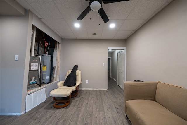 living area with water heater, a drop ceiling, hardwood / wood-style flooring, and ceiling fan