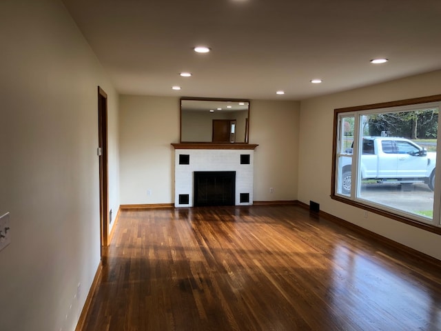 unfurnished living room featuring a brick fireplace and dark hardwood / wood-style floors