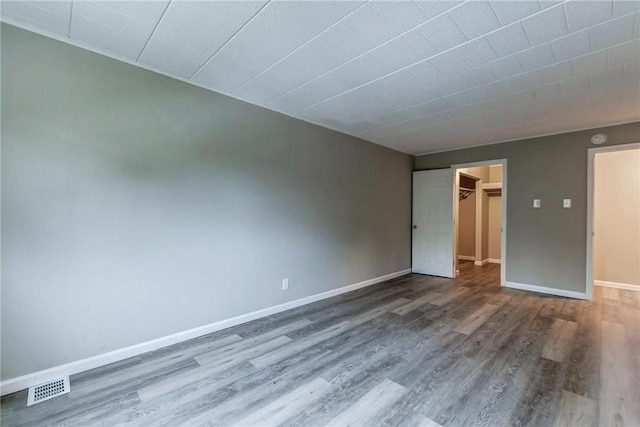empty room featuring wood finished floors, visible vents, and baseboards