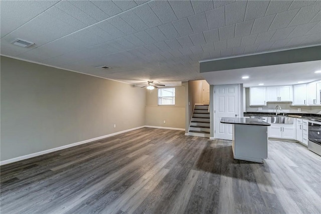 kitchen with dark countertops, a sink, baseboards, open floor plan, and dark wood-type flooring