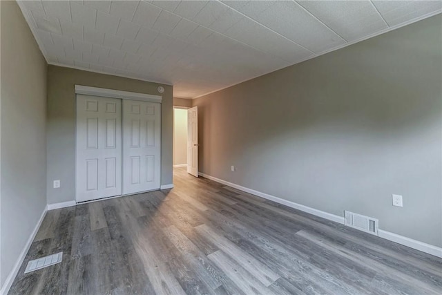 unfurnished bedroom featuring a closet, visible vents, wood finished floors, and baseboards
