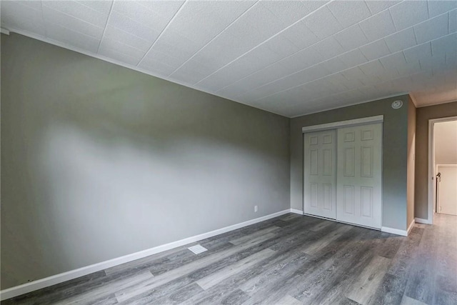 unfurnished bedroom featuring baseboards, dark wood-style flooring, and a closet