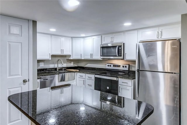kitchen featuring appliances with stainless steel finishes, dark stone counters, white cabinetry, and a sink