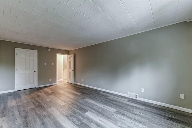 spare room with baseboards, visible vents, and wood finished floors