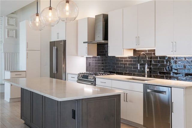 kitchen featuring white cabinetry, wall chimney exhaust hood, appliances with stainless steel finishes, and decorative light fixtures