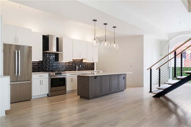 kitchen with wall chimney exhaust hood, hanging light fixtures, stainless steel appliances, light wood-type flooring, and white cabinets