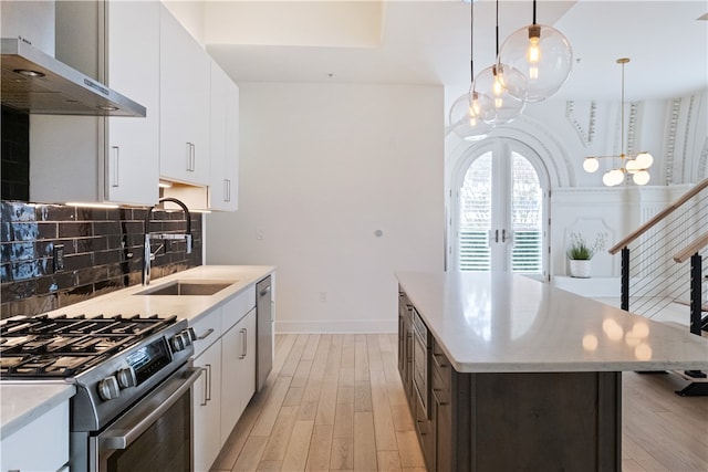 kitchen with white cabinetry, stainless steel appliances, wall chimney range hood, and decorative light fixtures