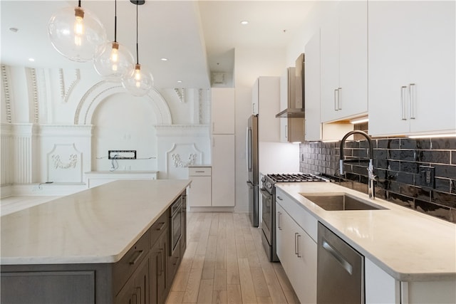 kitchen featuring appliances with stainless steel finishes, sink, hanging light fixtures, light hardwood / wood-style floors, and white cabinets