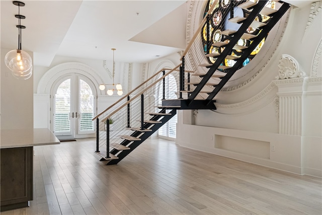 stairs with an inviting chandelier, french doors, and wood-type flooring