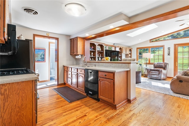 kitchen featuring decorative backsplash, dishwasher, light hardwood / wood-style floors, lofted ceiling with skylight, and sink