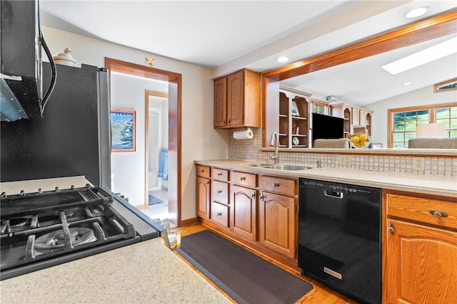 kitchen with decorative backsplash, light hardwood / wood-style flooring, stainless steel appliances, sink, and vaulted ceiling with skylight