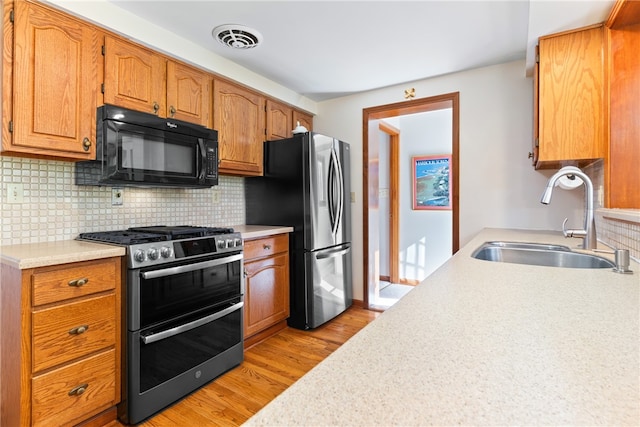 kitchen featuring stainless steel appliances, decorative backsplash, sink, and light wood-type flooring