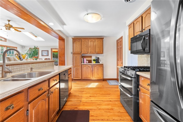 kitchen with sink, a skylight, stainless steel appliances, decorative backsplash, and light hardwood / wood-style flooring