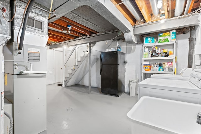 basement featuring sink, heating unit, separate washer and dryer, and black fridge