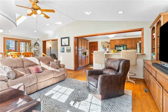 living room featuring light hardwood / wood-style floors, vaulted ceiling with skylight, and ceiling fan