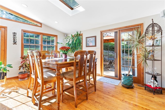 dining space with vaulted ceiling with skylight and light hardwood / wood-style floors