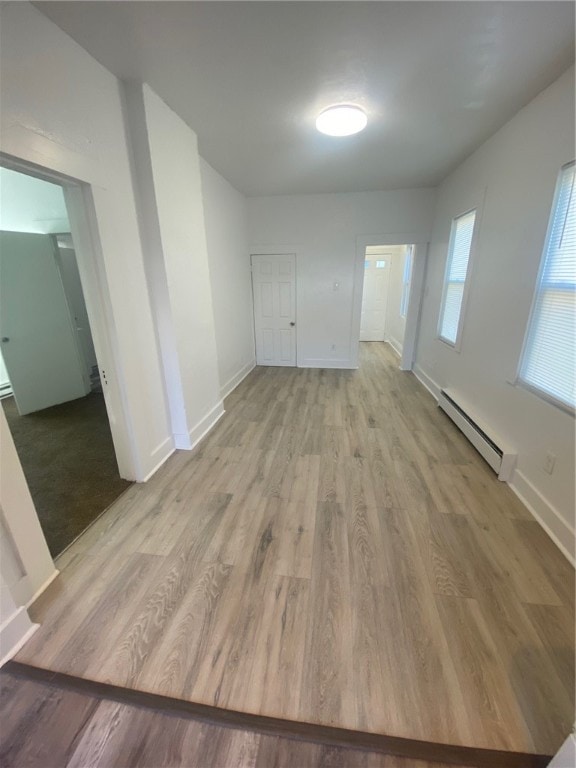 unfurnished room featuring a baseboard heating unit and light hardwood / wood-style floors