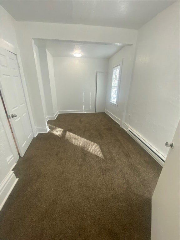 empty room featuring a baseboard heating unit and dark carpet