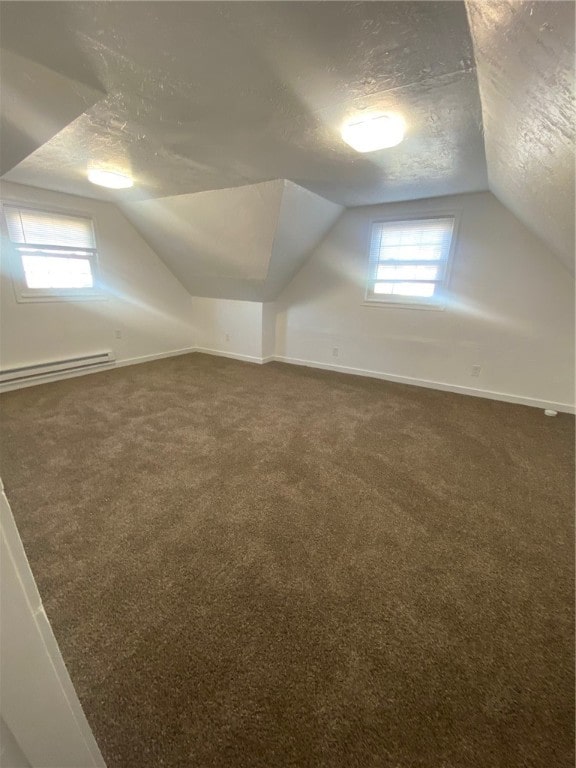 bonus room with a baseboard heating unit, dark colored carpet, a textured ceiling, and vaulted ceiling