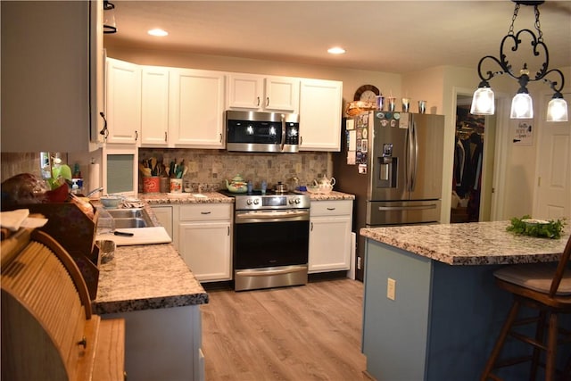 kitchen featuring pendant lighting, white cabinets, a kitchen breakfast bar, light hardwood / wood-style flooring, and appliances with stainless steel finishes