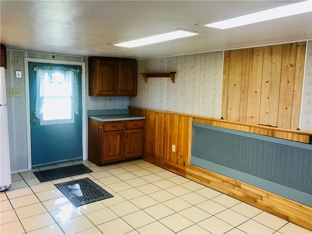 kitchen featuring radiator, light tile patterned floors, wooden walls, and white refrigerator