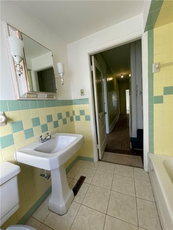 bathroom with toilet, tile walls, a tub, and tile patterned flooring