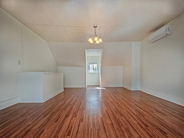 bonus room with an inviting chandelier, hardwood / wood-style flooring, an AC wall unit, and vaulted ceiling