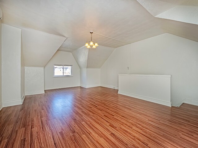 bonus room featuring a textured ceiling, wood-type flooring, vaulted ceiling, and a chandelier