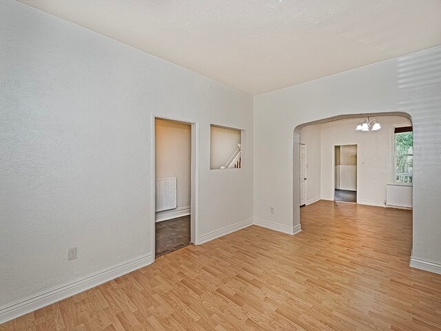 empty room with a chandelier, radiator heating unit, and light hardwood / wood-style floors