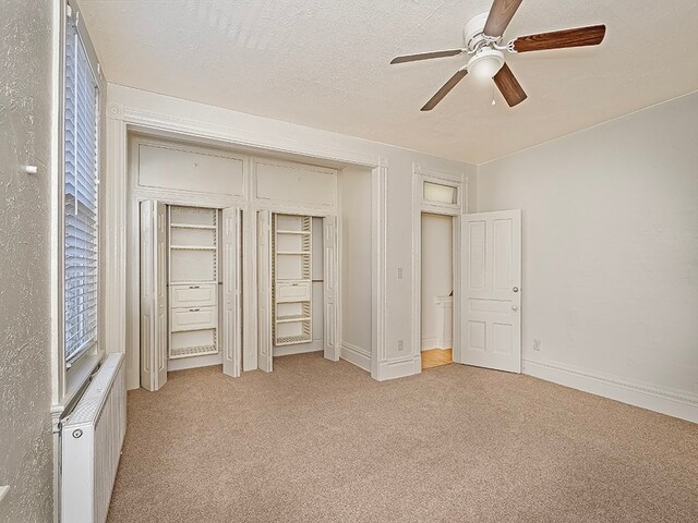 unfurnished bedroom with a textured ceiling, radiator heating unit, light colored carpet, and ceiling fan