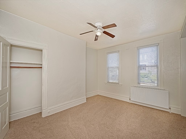 unfurnished bedroom with radiator, ceiling fan, light carpet, and a closet