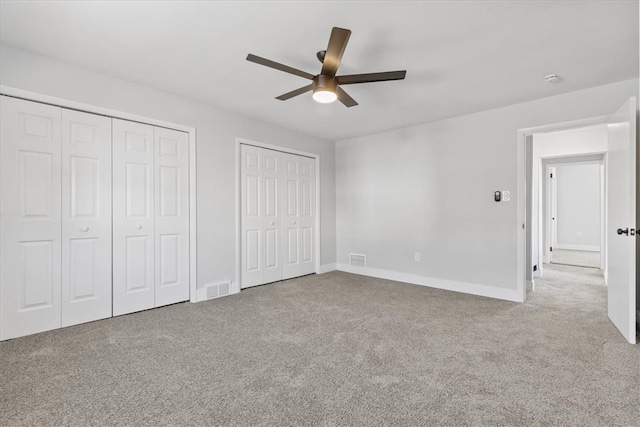 unfurnished bedroom with ceiling fan, light carpet, and two closets