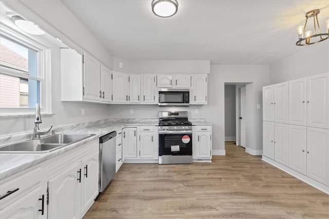 kitchen featuring sink, an inviting chandelier, light wood-type flooring, white cabinetry, and appliances with stainless steel finishes