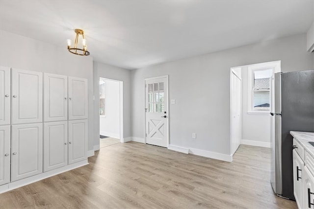 interior space featuring white cabinetry, a notable chandelier, light wood-type flooring, and stainless steel fridge