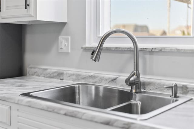 room details with white cabinets, sink, and light stone counters