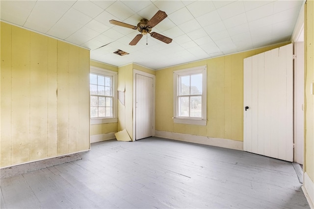 unfurnished bedroom featuring light hardwood / wood-style flooring, wooden walls, and ceiling fan