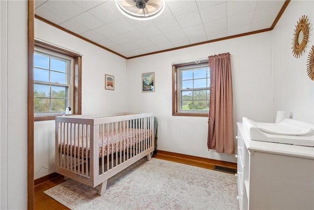 bedroom with ornamental molding, wood-type flooring, multiple windows, and a crib