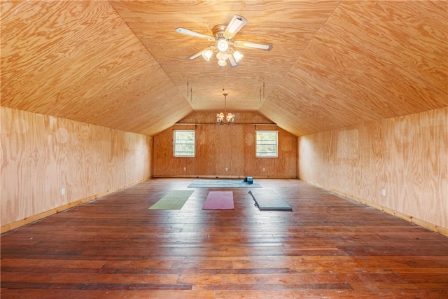 additional living space with wood walls, hardwood / wood-style flooring, ceiling fan with notable chandelier, and vaulted ceiling